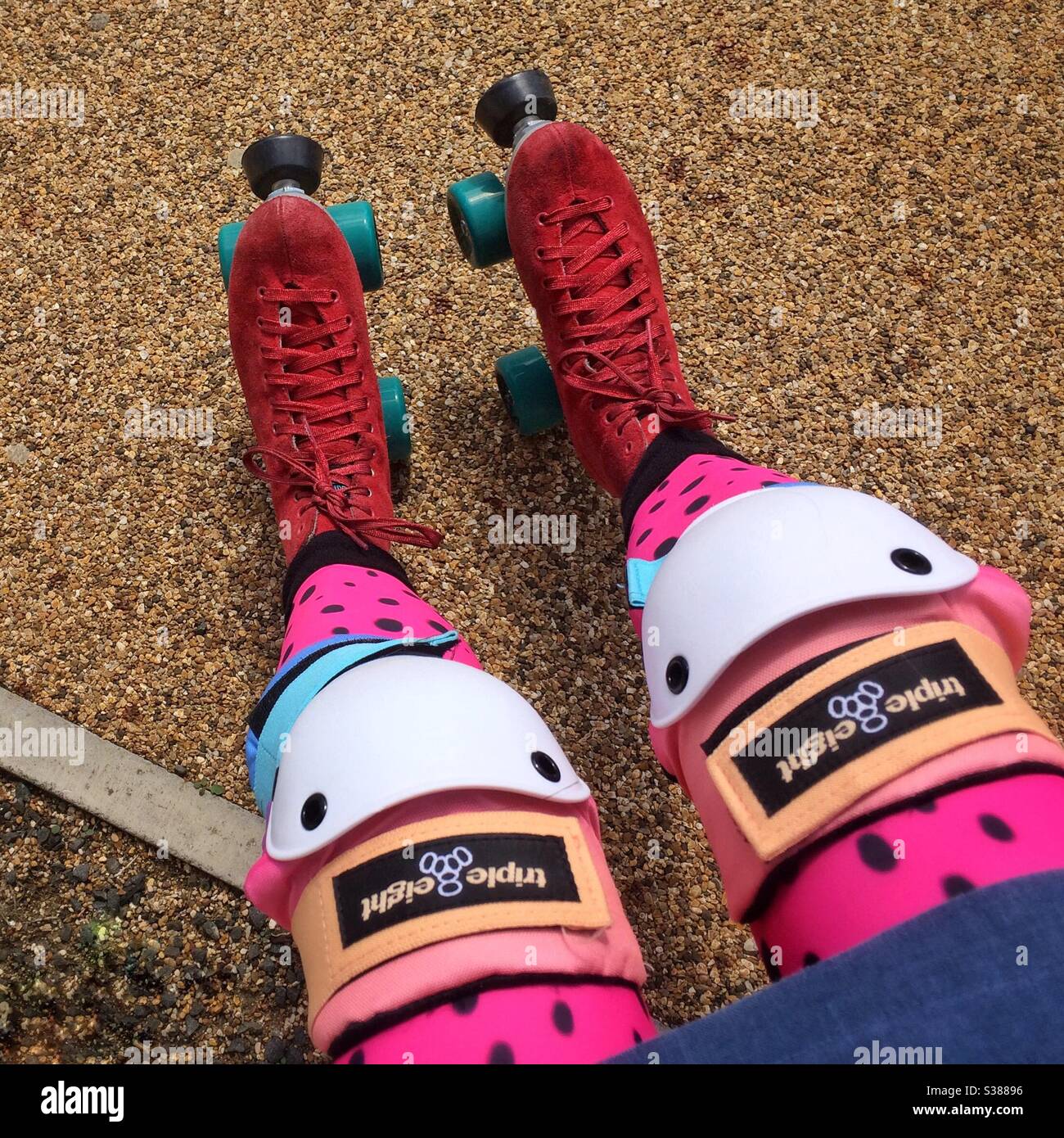 A woman’s legs and feet wearing red suede roller skates and colourful protective knee pads, POV looking down, seated. - Smartphone Captured Stock Image