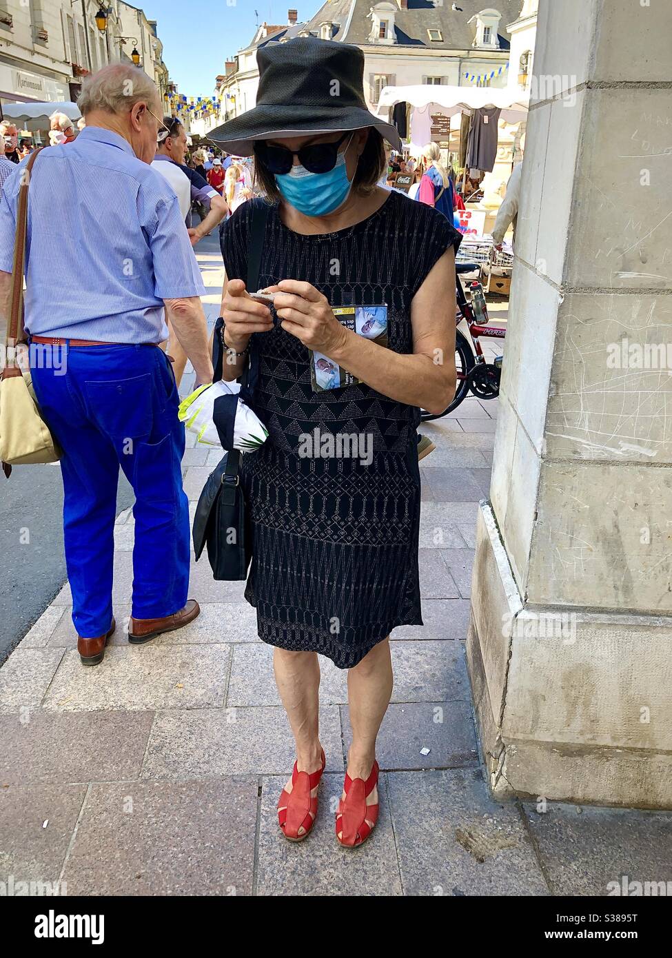 Woman in crowded street wearing face mask hand-rolling a cigarette - France. Stock Photo