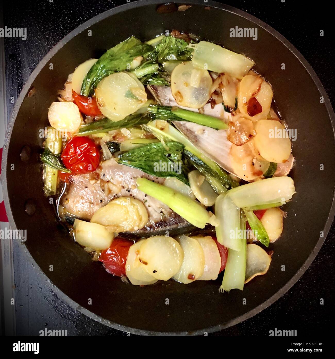 Cooking at home: fish pot with salmon, potatoes, cherry tomatoes, vegetables in olive oil - Smartphone Captured Stock Image