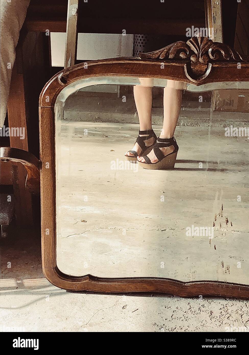 Reflection of girl’s legs and platform sandals in an antique mirror incased in a wood frame. Stock Photo