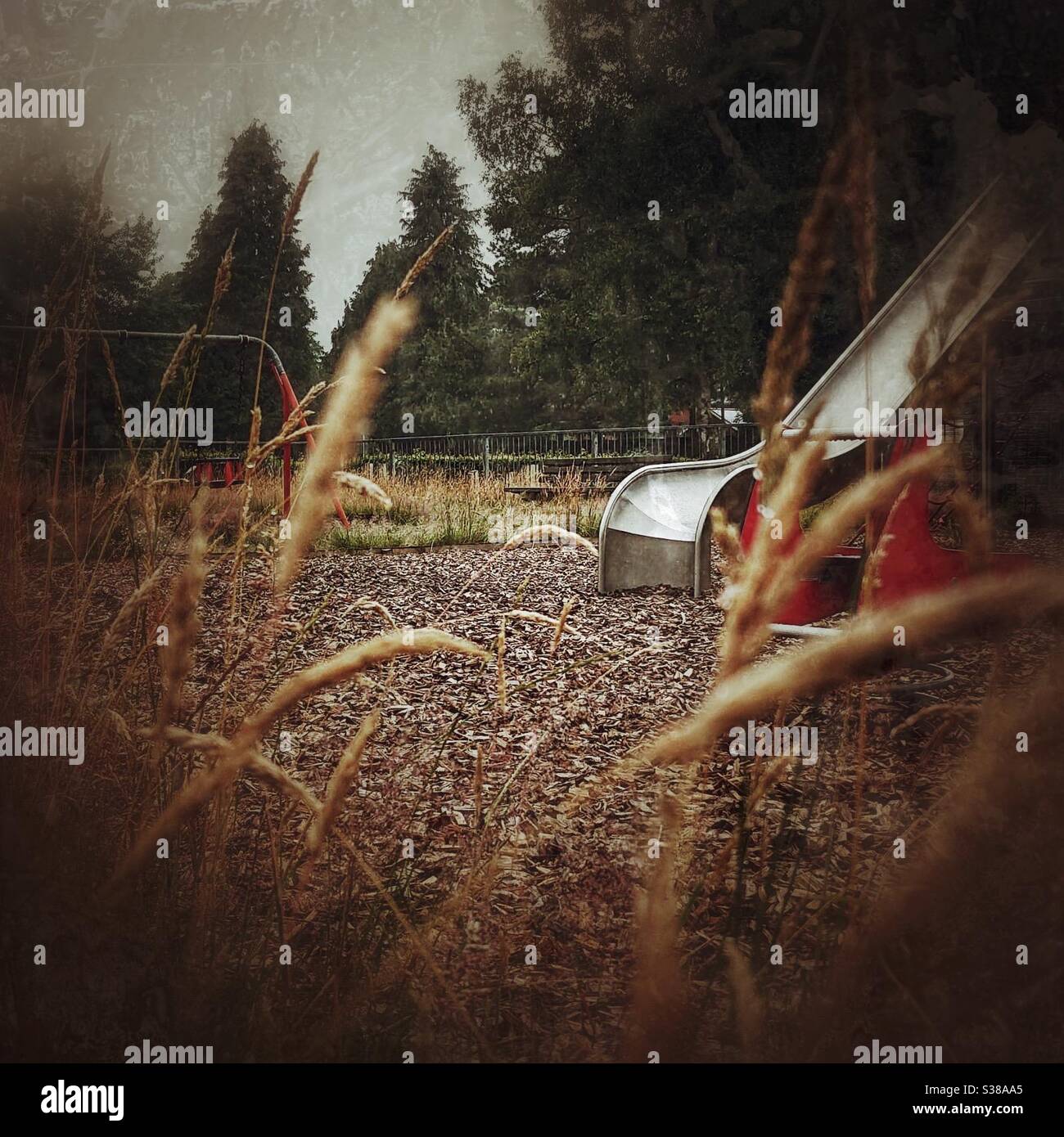 A photograph of a disused overgrown playground during COVID-19 lockdown quarantine. Slide and swings abandoned - Smartphone Captured Stock Image
