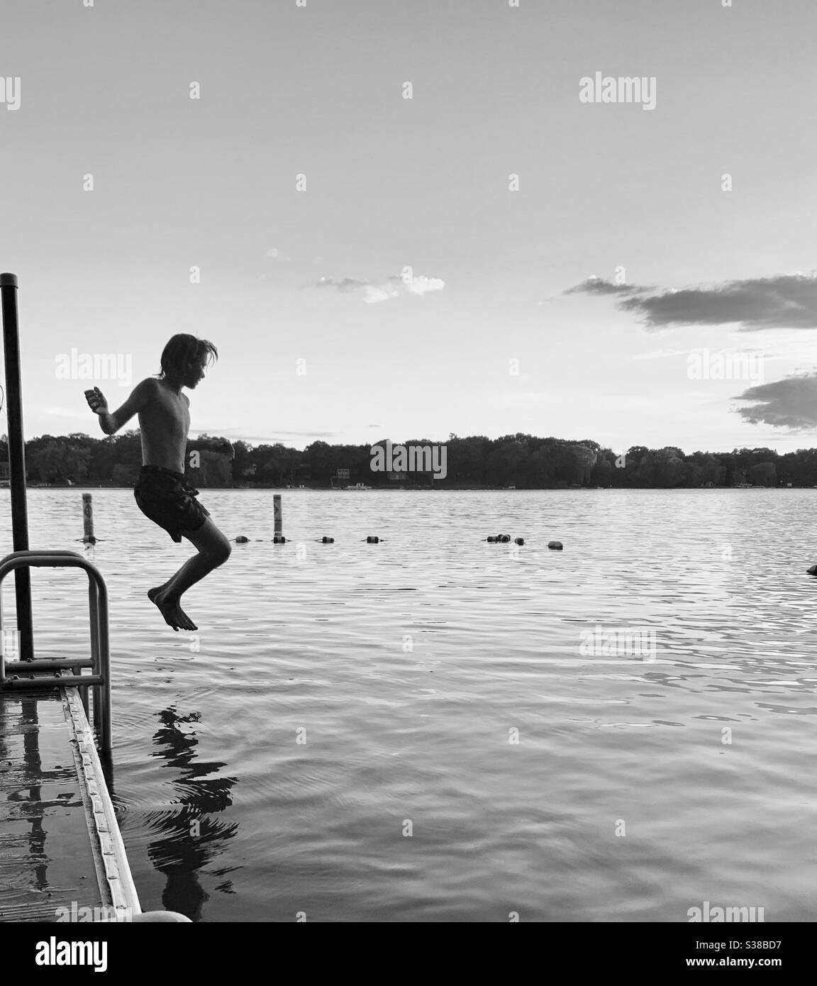 Teen boy jumping off pier into small lake. Stock Photo