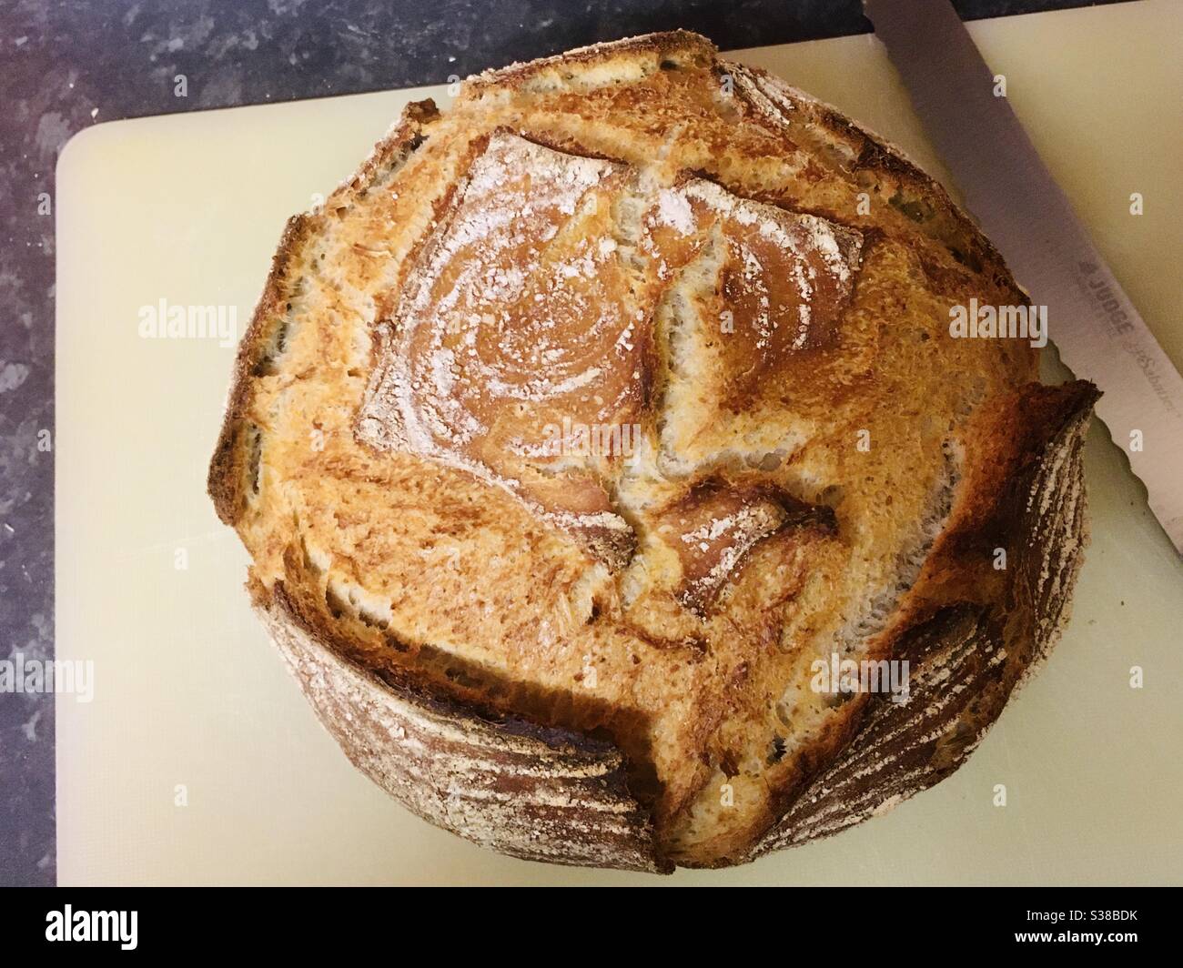 Freshly home baked sourdough loaf on a white chopping board next to a knife - rustic, artisan baking Stock Photo
