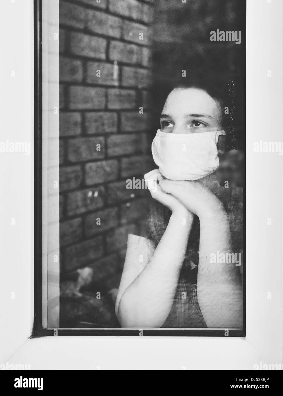 Teen girl wearing white face mask looking out window Stock Photo
