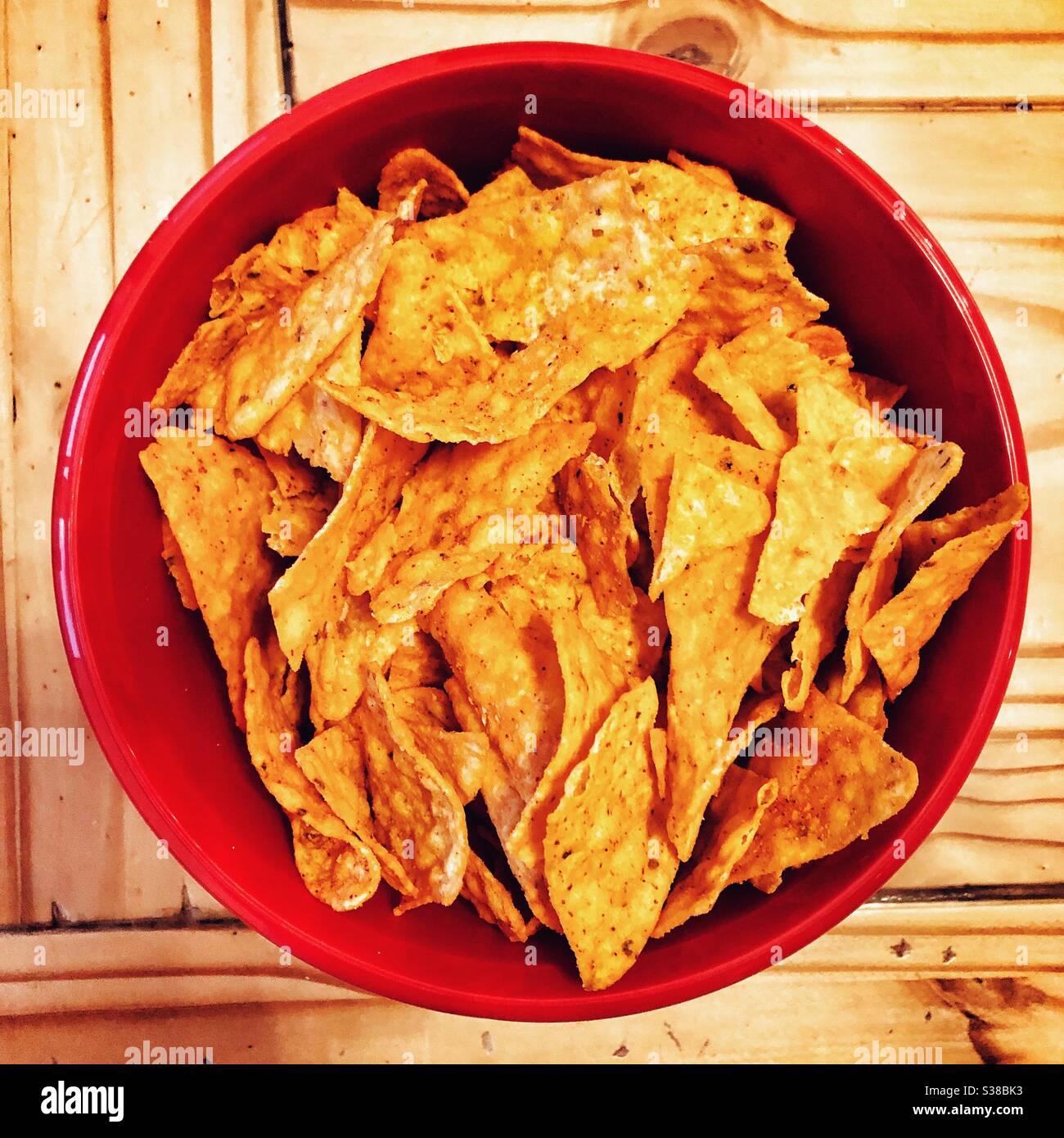 Nacho cheese Doritos in a red bowl on wooden table Stock Photo