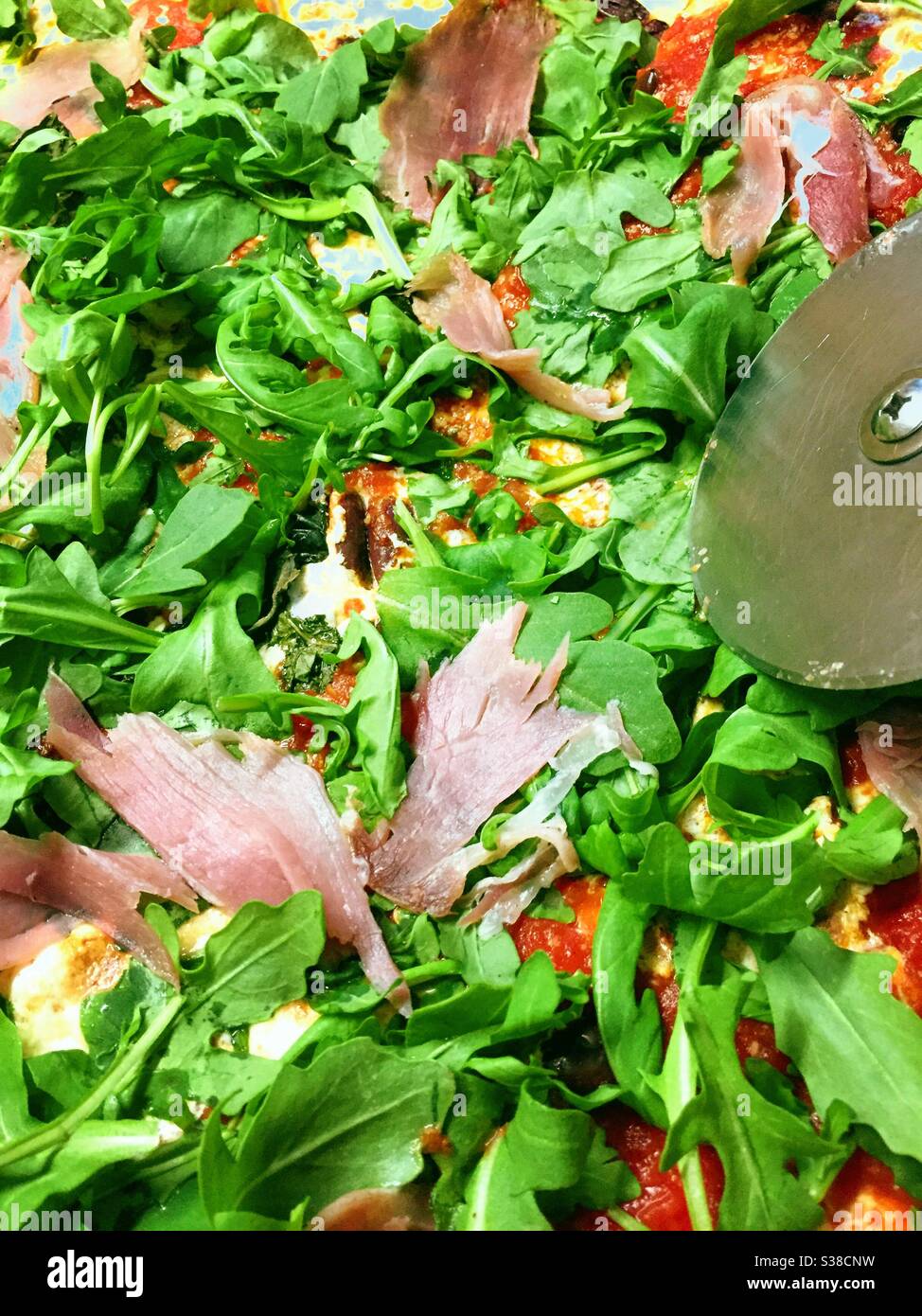 Close up of a metal pizza wheel cutting a slice of gourmet prosciutto and arugula pizza, USA - Smartphone Captured Stock Image