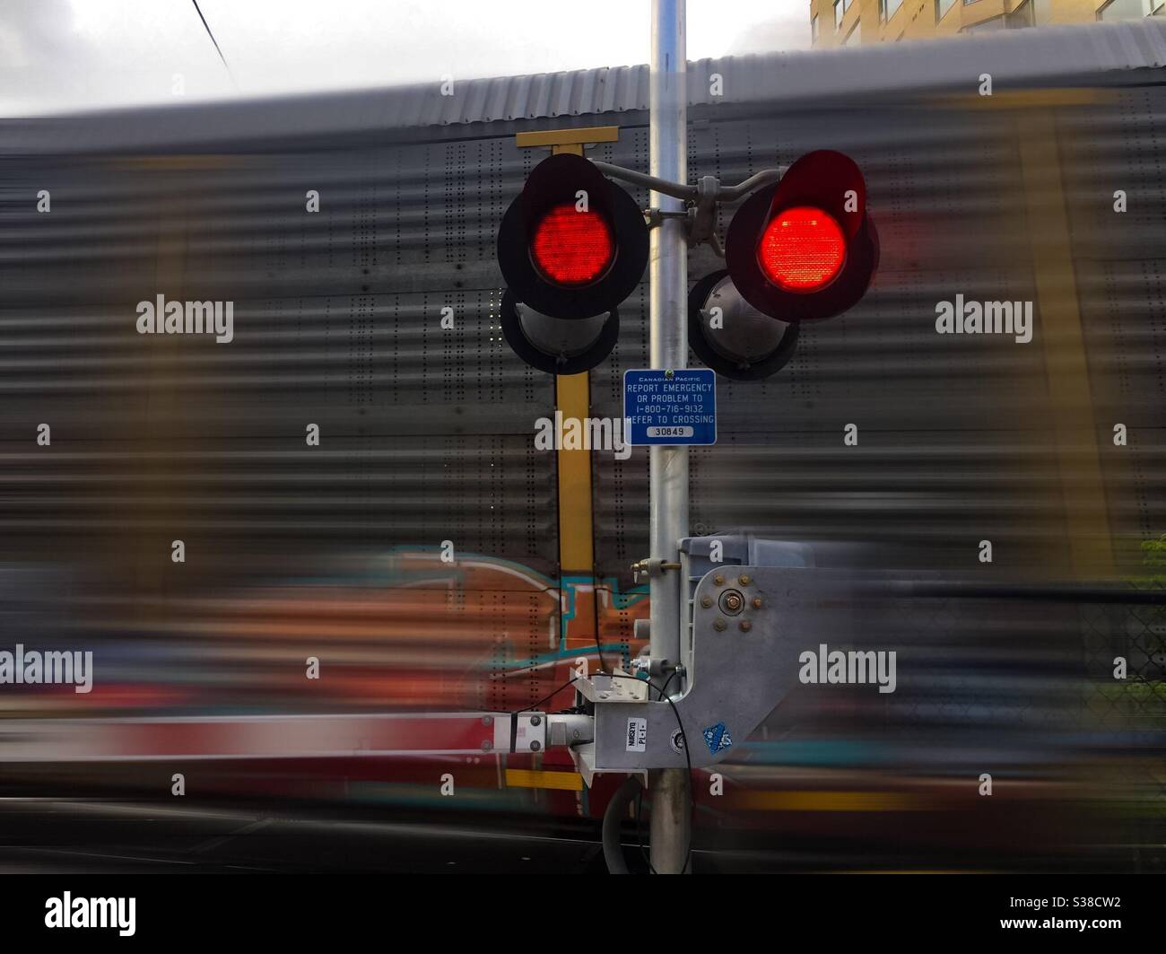Moving train at a railway crossing with flashing red lights on a cloudy day, Ontario, Canada. Stock Photo