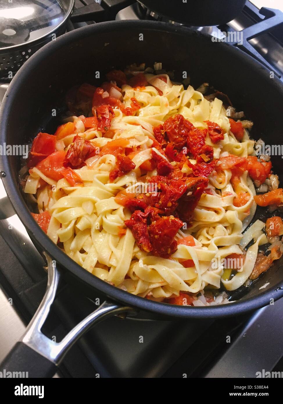 A pasta dish fettuccine with sun-dried tomato pasta being prepared in a stove top skillet in a residential kitchen, USA - Smartphone Captured Stock Image