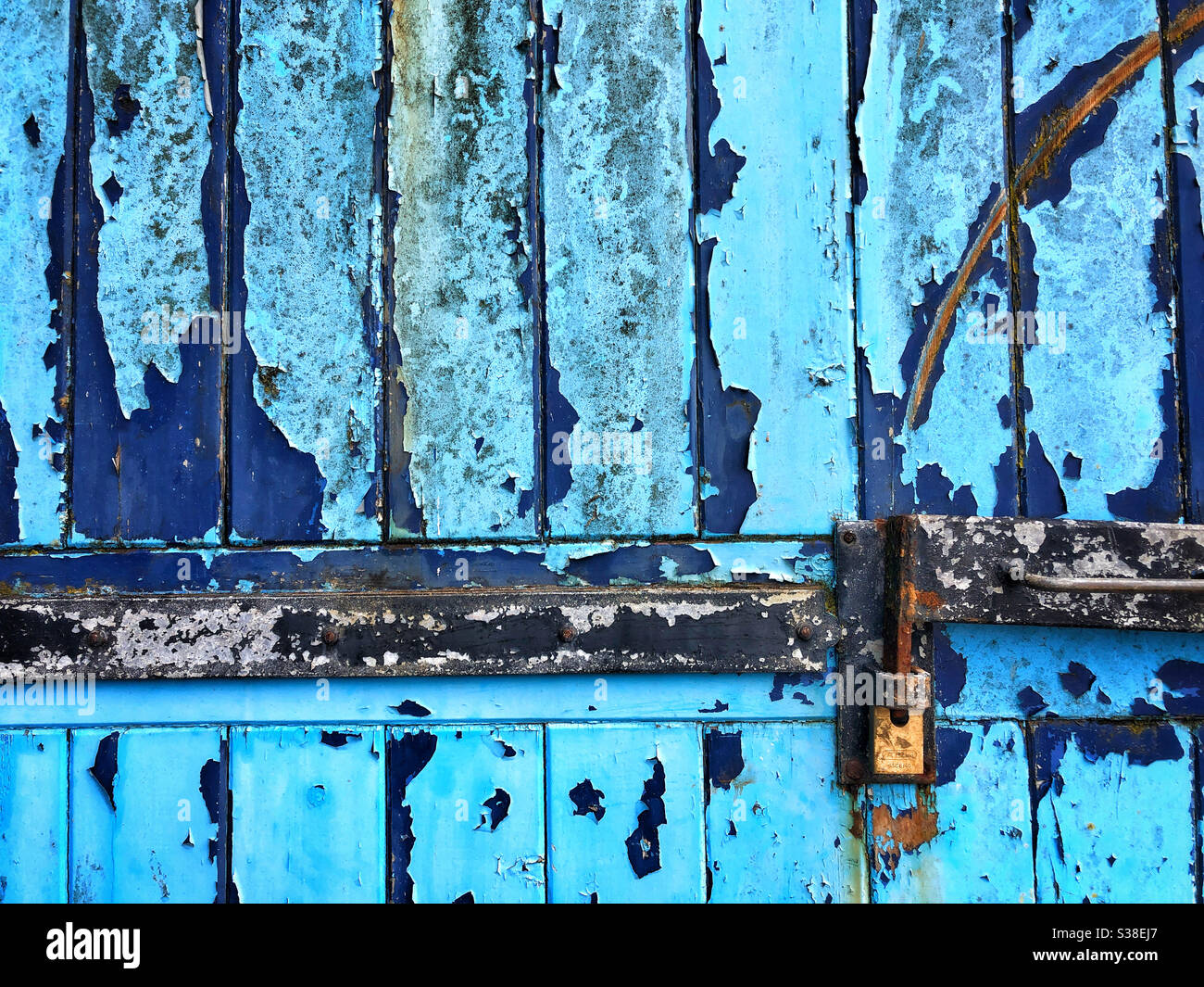 Textured old garage door with flaky blue paint and padlock Stock Photo