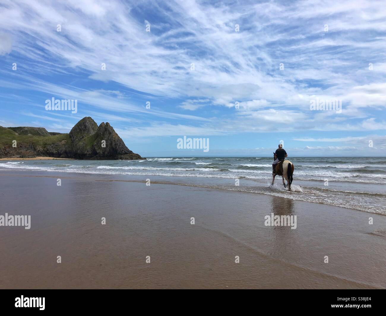 A lone male horse rider in the sea at Three Cliffs Bay, Gower, Swansea, Wales, August. Stock Photo