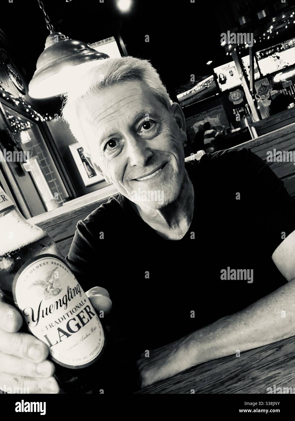 Older man sitting in a restaurant smiling and holding a bottle of beer. - Smartphone Captured Stock Image
