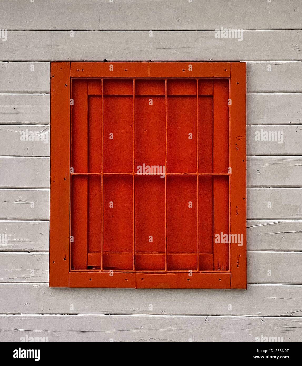 A Window with bars, is blocked up for security and painted in bright orange and set in a white painted wooden framework Stock Photo