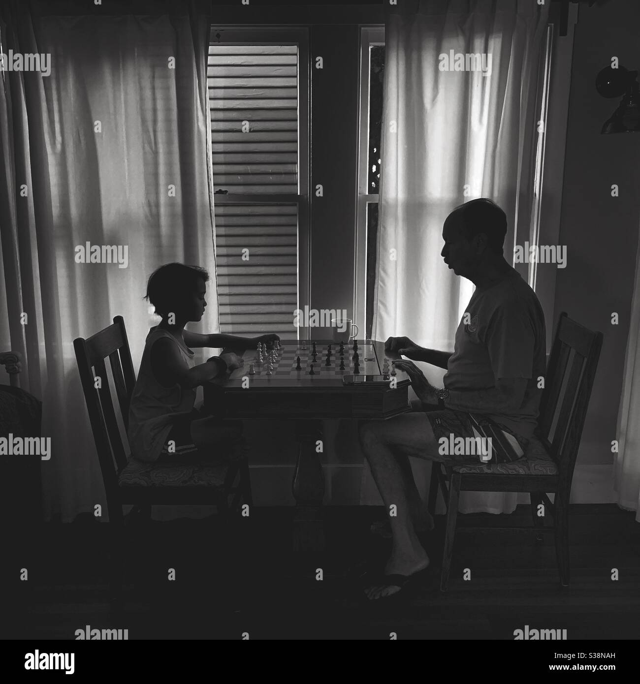 Black and white silhouette image of a man teaching a boy how to play chess. Stock Photo