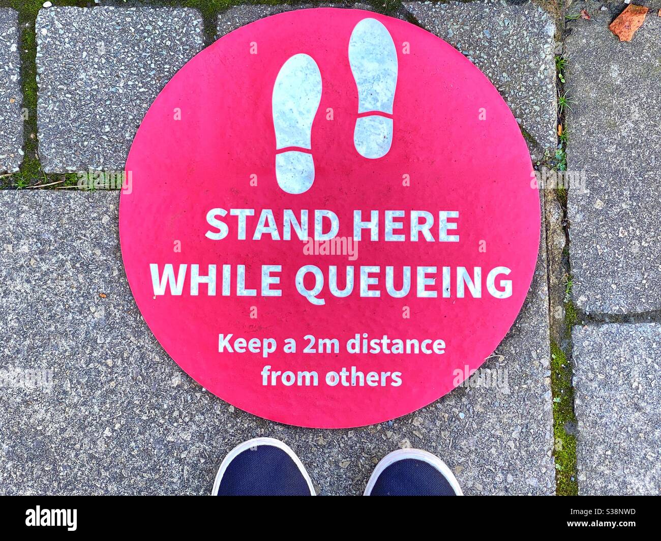 Social distancing sign on the ground with a person’s feet below it Stock Photo