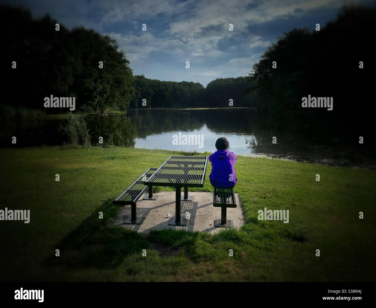 A woman watches a lake sitting in a park - Smartphone Captured Stock Image