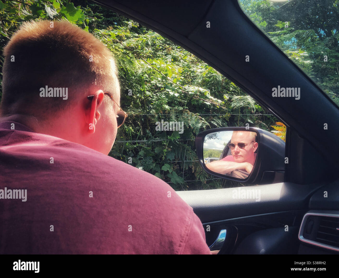 Young man looking out of a car window and reflected in the wing mirror. - Smartphone Captured Stock Image