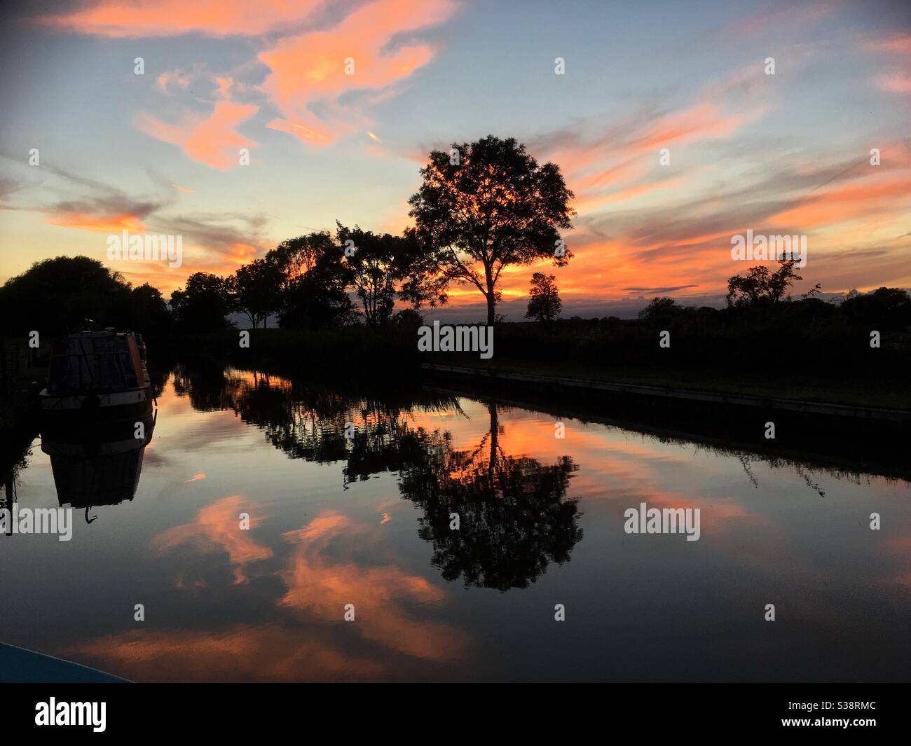 Colourful canal sunset and reflection on water with silhouette of tree line and hedge - Smartphone Captured Stock Image