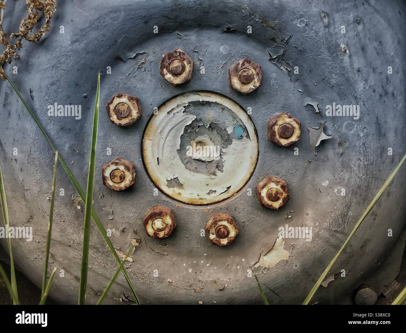 Old hub of tractor wheel in grass, with desaturated colour and rusted bolts, wheelnuts, wheel nuts Stock Photo