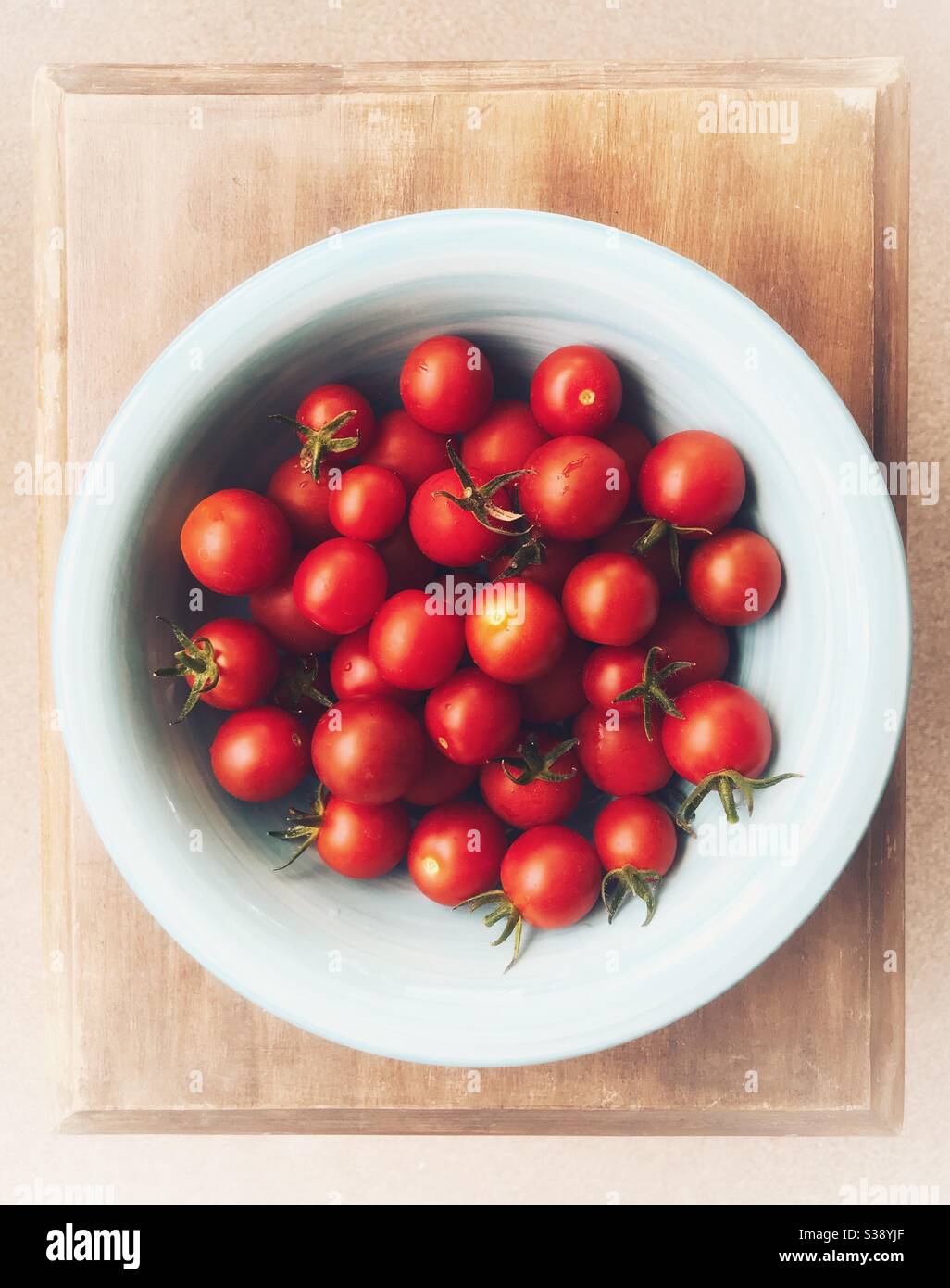 Cherry tomatoes in a blue bowl on a small wood table - Smartphone Captured Stock Image