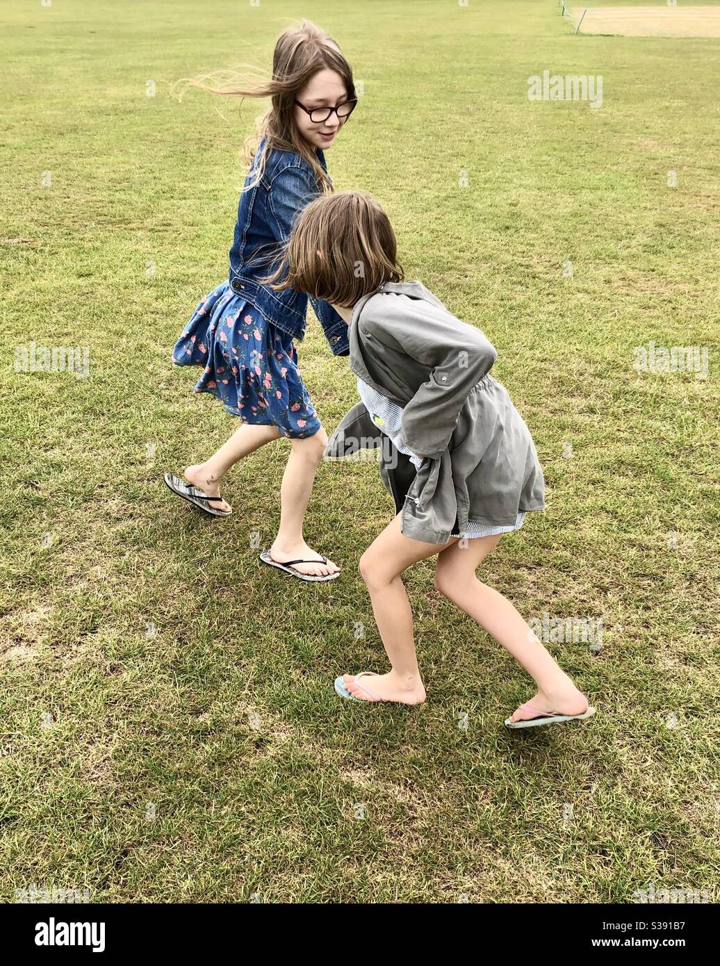 Two sisters play fighting on a field - Smartphone Captured Stock Image
