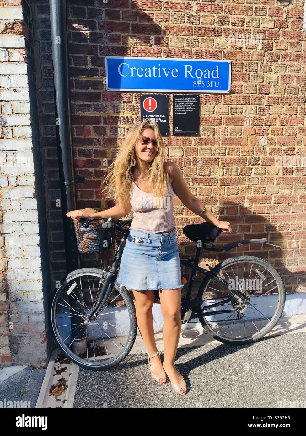 Woman and bike in front of sign saying creative road - Smartphone Captured Stock Image