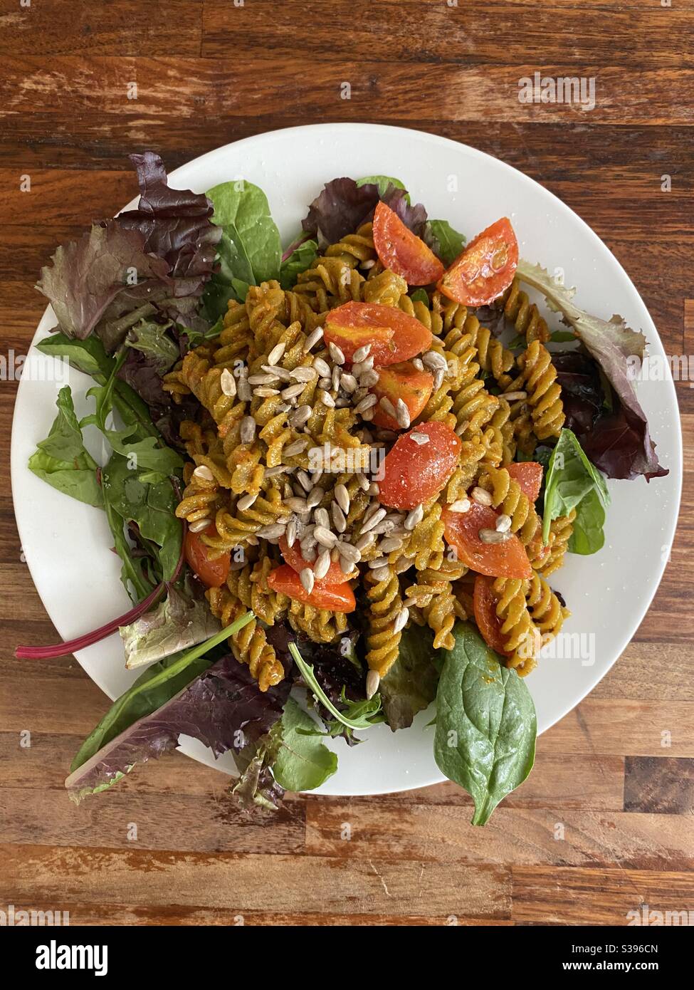 Pea protein pasta in vegan pesto with side salad and tomatoes, sprinkled with sunflower seeds Stock Photo