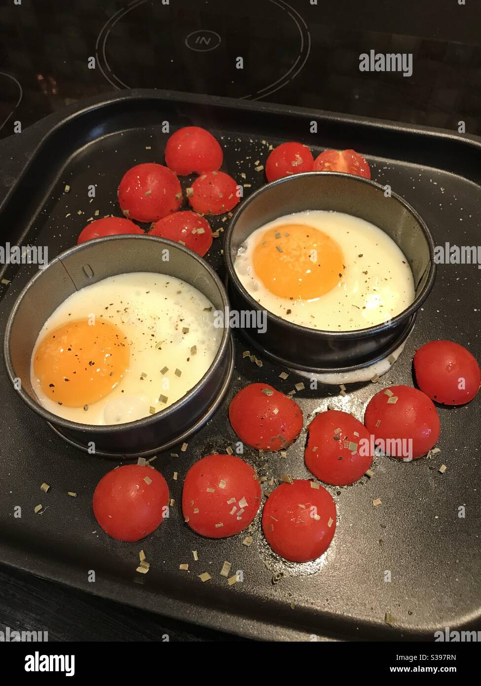 Fried eggs in circular ring with tomato tomatoes and herbs on baking tray - Smartphone Captured Stock Image