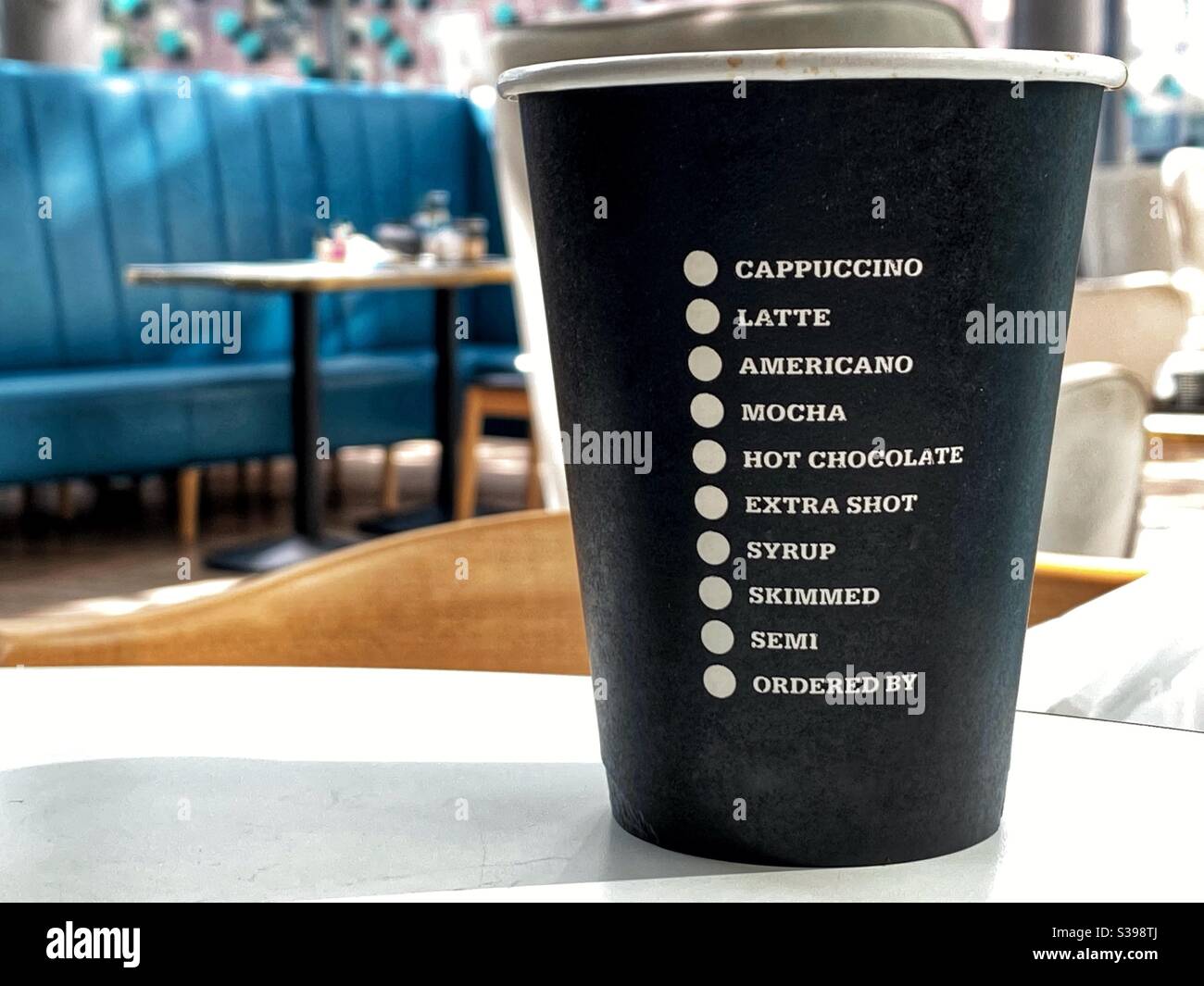 Disposable coffee cup on a table with list of coffees and options. No people. Stock Photo