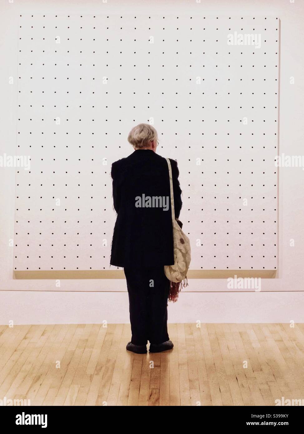 Visitor on black coat at art gallery in front of Bridget Riley white ...