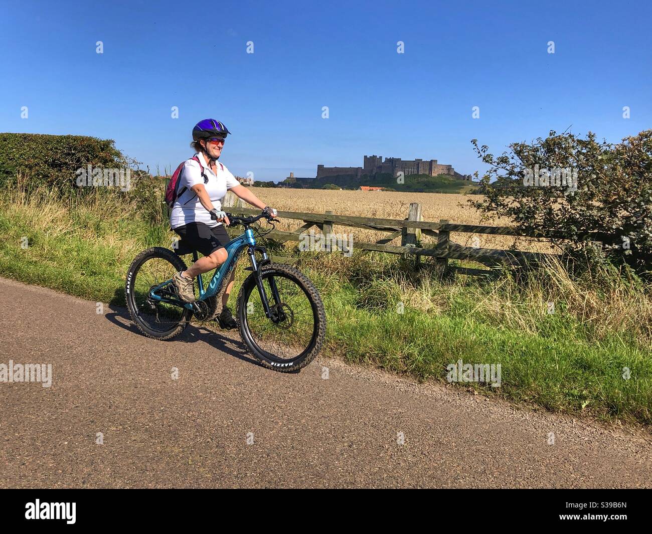 Woman riding eBike pass Bamburgh Castle - Smartphone Captured Stock Image