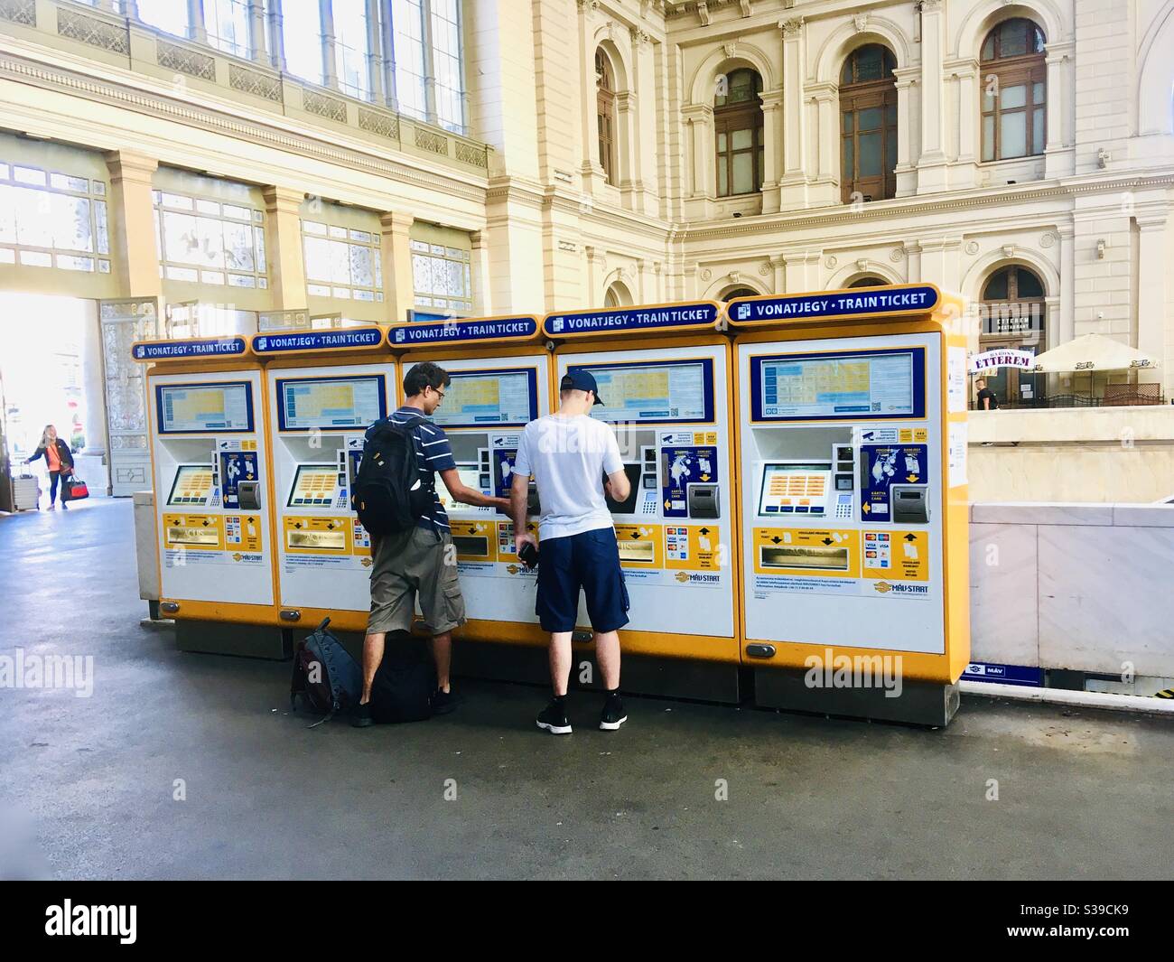 Young men buying train ticket from ticket machine at Keleti palyaudvar (Keleti Railway Station), Budapest, Hungary - Smartphone Captured Stock Image