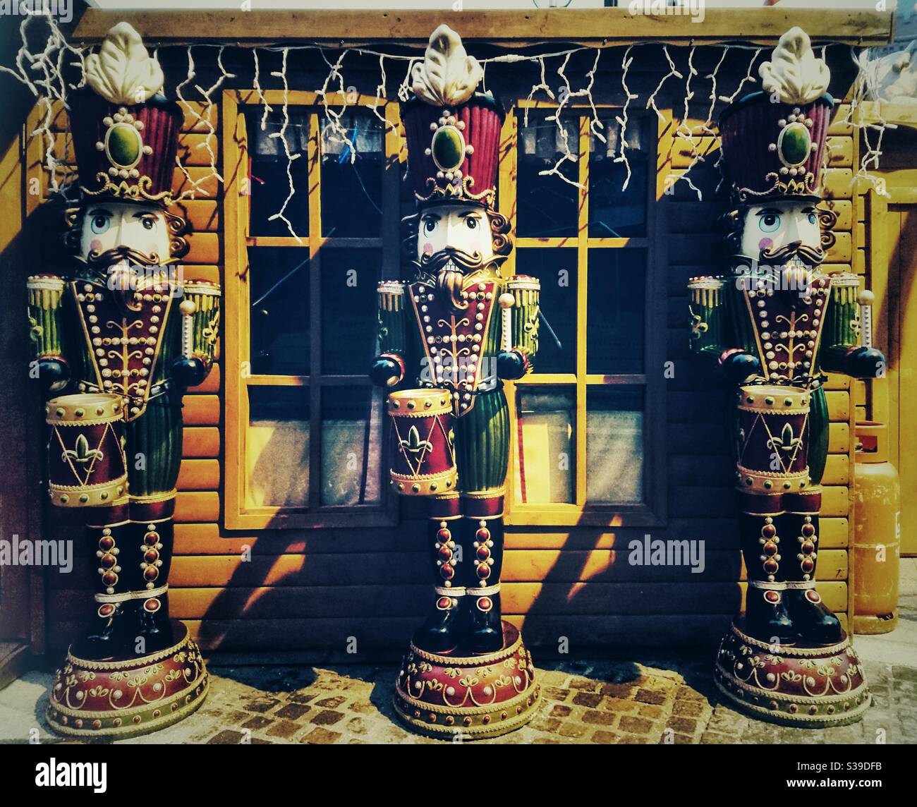 A photograph of festive Christmas soldier drummer figurines, outside a Christmas grotto with fairy lights. - Smartphone Captured Stock Image