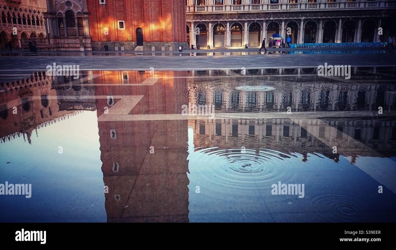 A photograph of high water (acqua alta) coming up through drains in St Mark’s square in Venice, Italy. Beautiful reflections of the buildings and the campanile bell tower. - Smartphone Captured Stock Image