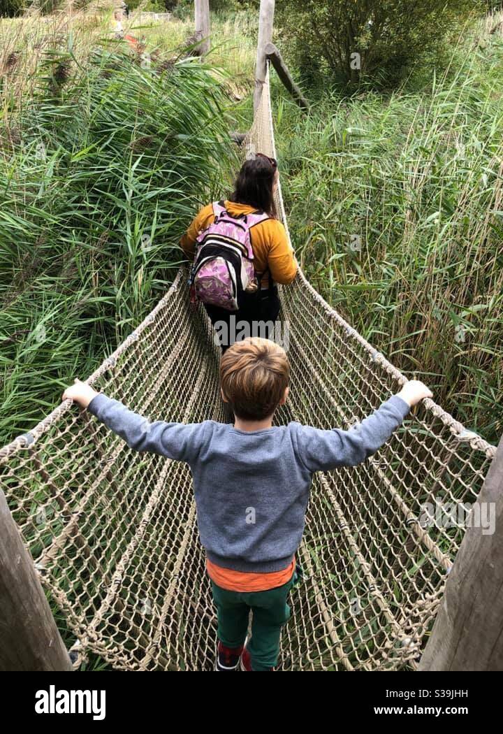A child following a woman over a rope bridge Stock Photo