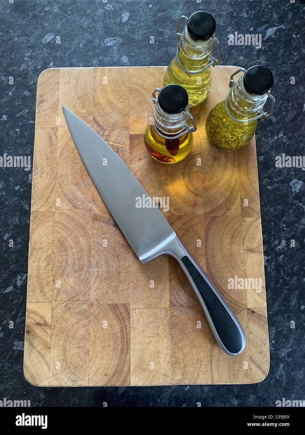 Chef’s knife on butcher block chopping board with infused oils in small glass bottles Stock Photo