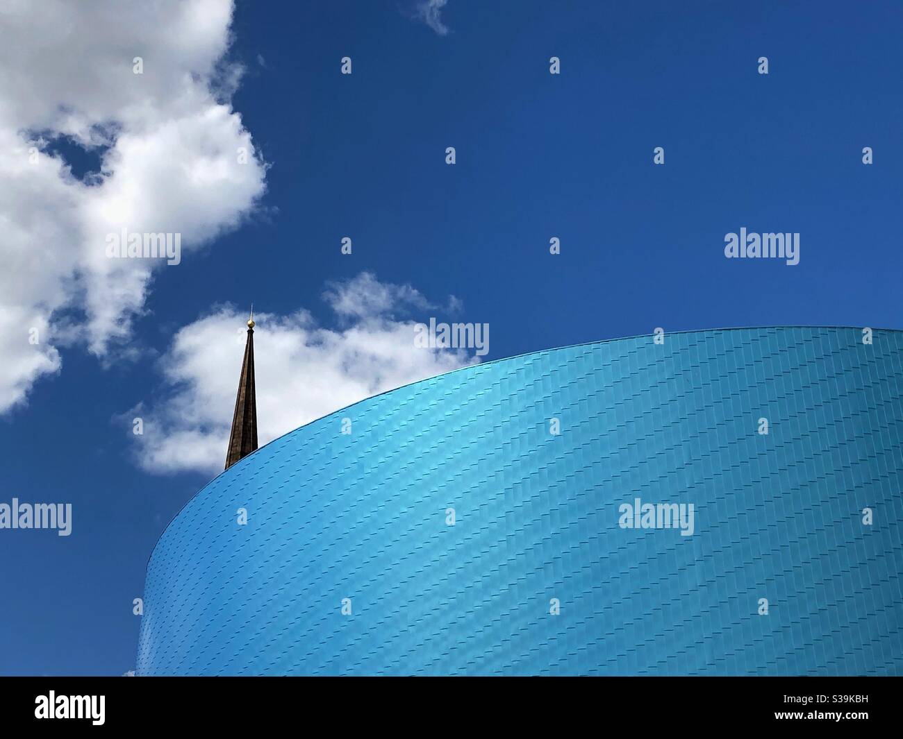Part of the characteristic circular facade of The Wave, an indoor water park with a church spire sticking up behind it in Coventry, West Midlands, UK. - Smartphone Captured Stock Image
