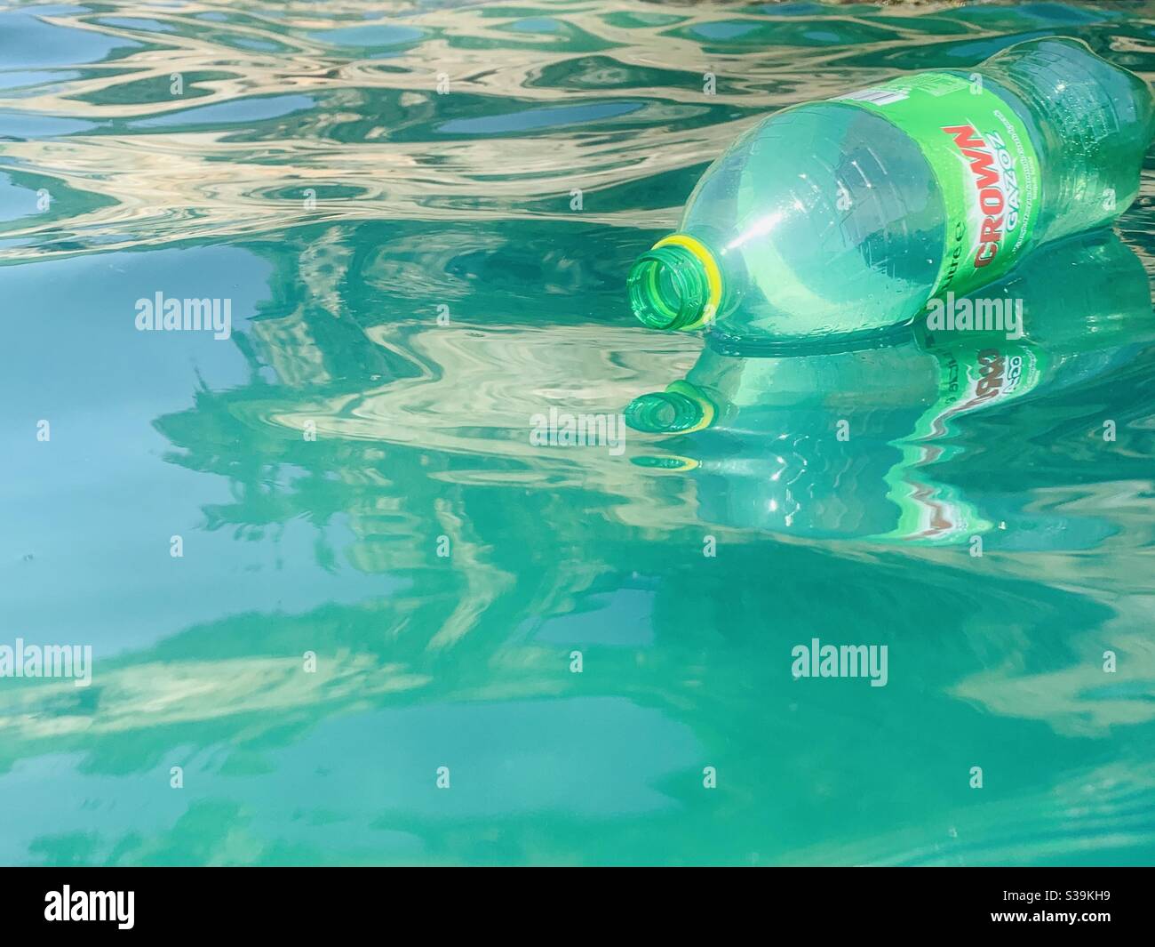 Bright green empty plastic bottle of crown floating on reflective waves Stock Photo