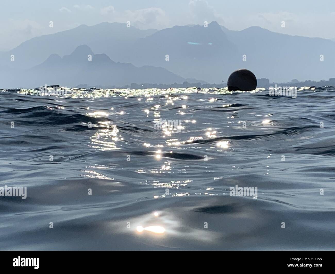 Sparkly water at Mermerli beach with round buoy silhouetted against mountains in the distance Stock Photo