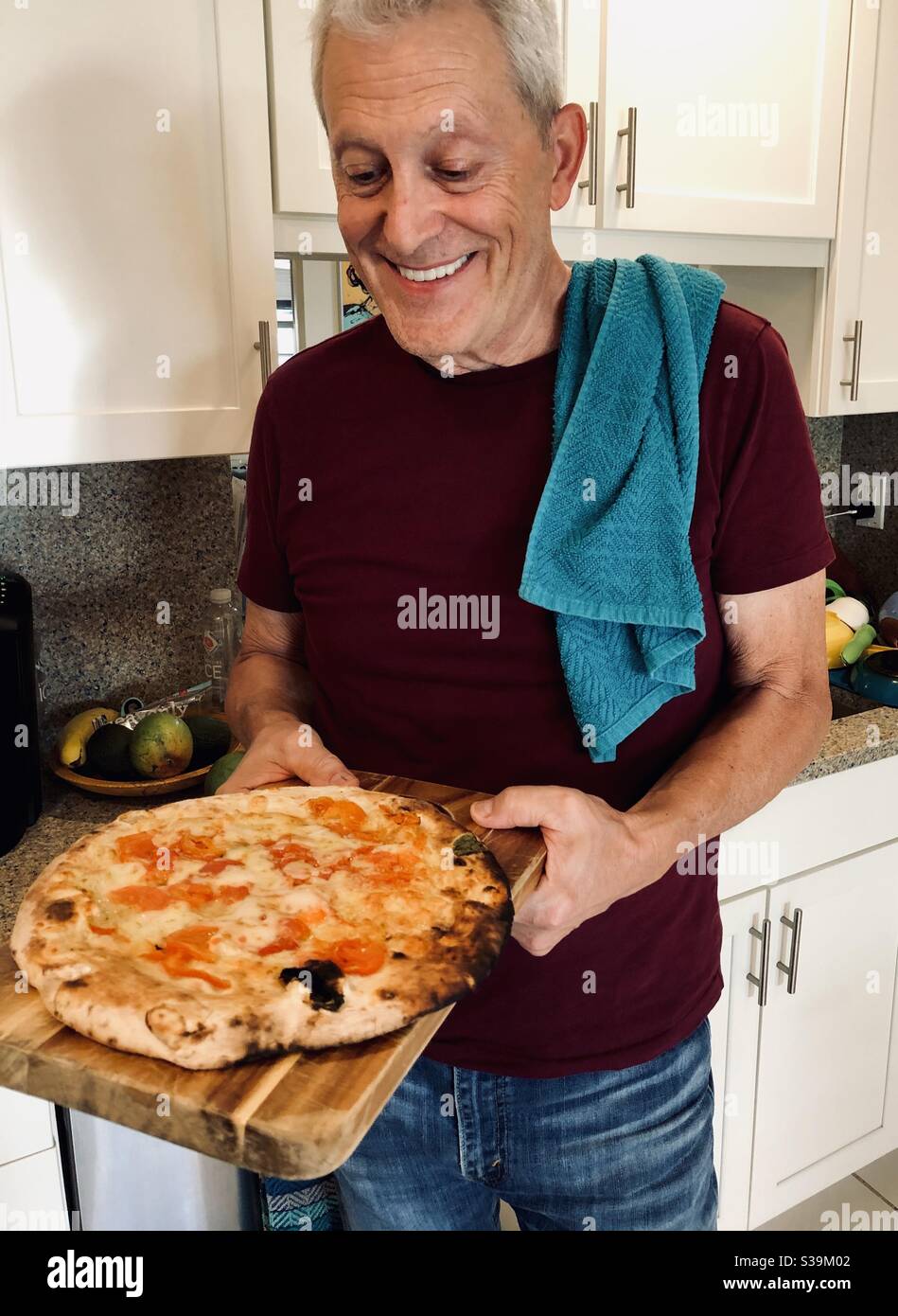 Happy man in kitchen about to eat a pizza just taken from the oven. - Smartphone Captured Stock Image