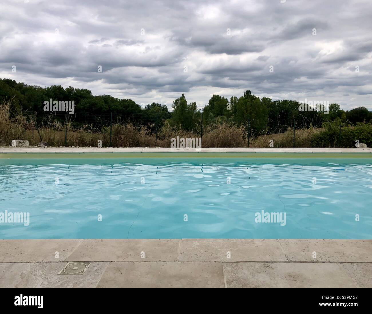 Contrast of blue swimming pool water and dark moody sky Stock Photo