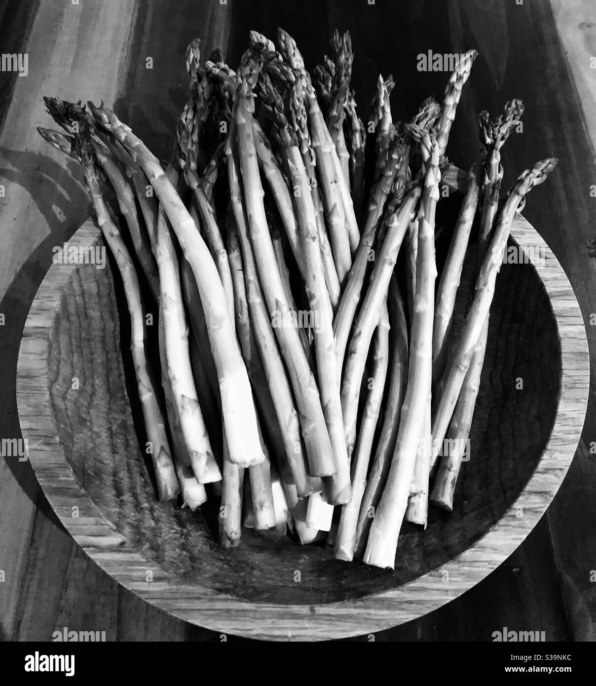 Monochromatic photograph of a bunch of asparagus in a wooden bowl on a wooden table. - Smartphone Captured Stock Image