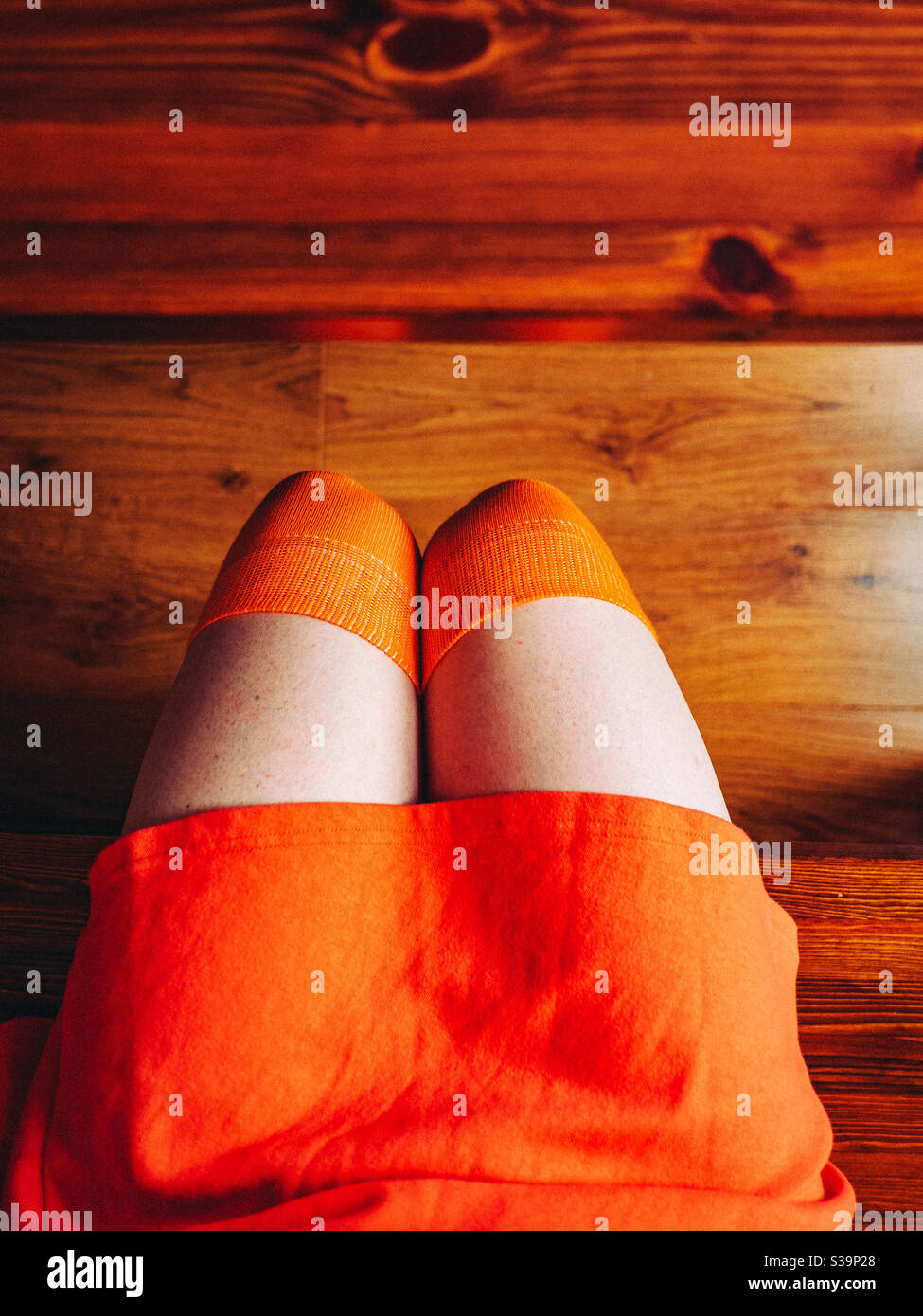 Woman sat wearing a orange skirt snd over the knee socks Stock Photo