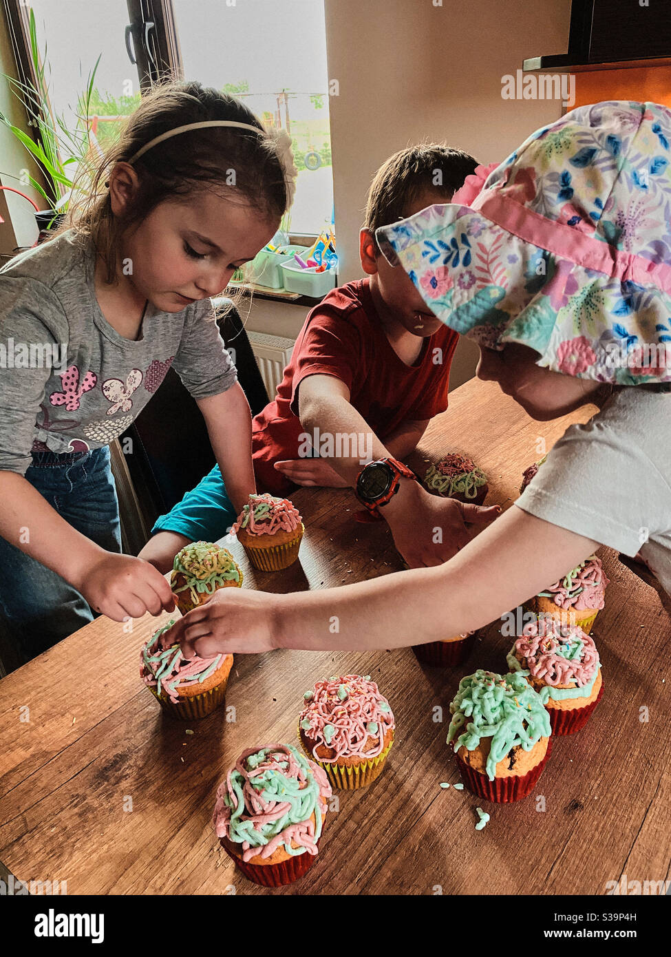Group of children baking cupcakes, preparing ingredients, toppings, sprinkles for decorating cookies. Kids learning to cook, working together in kitchen at home. Concept of happy family Stock Photo