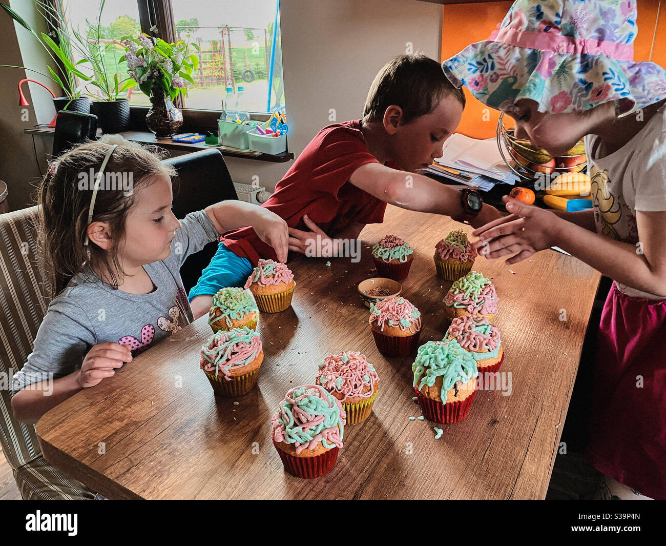 Group of children baking cupcakes, preparing ingredients, toppings, sprinkles for decorating cookies. Kids learning to cook, working together in kitchen at home. Concept of happy family Stock Photo