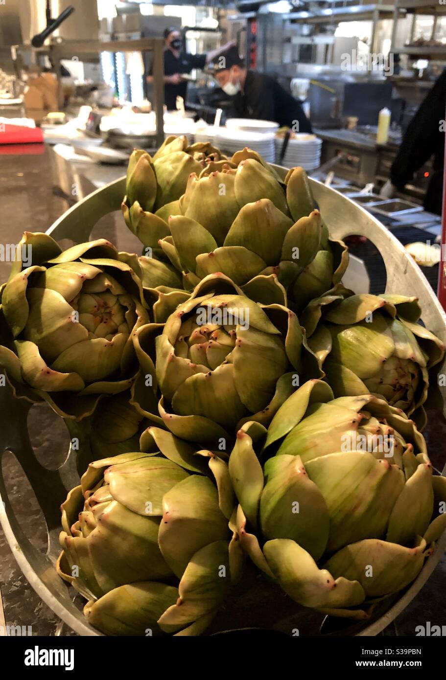Display of artichokes by an open restaurant kitchen with chefs working. - Smartphone Captured Stock Image