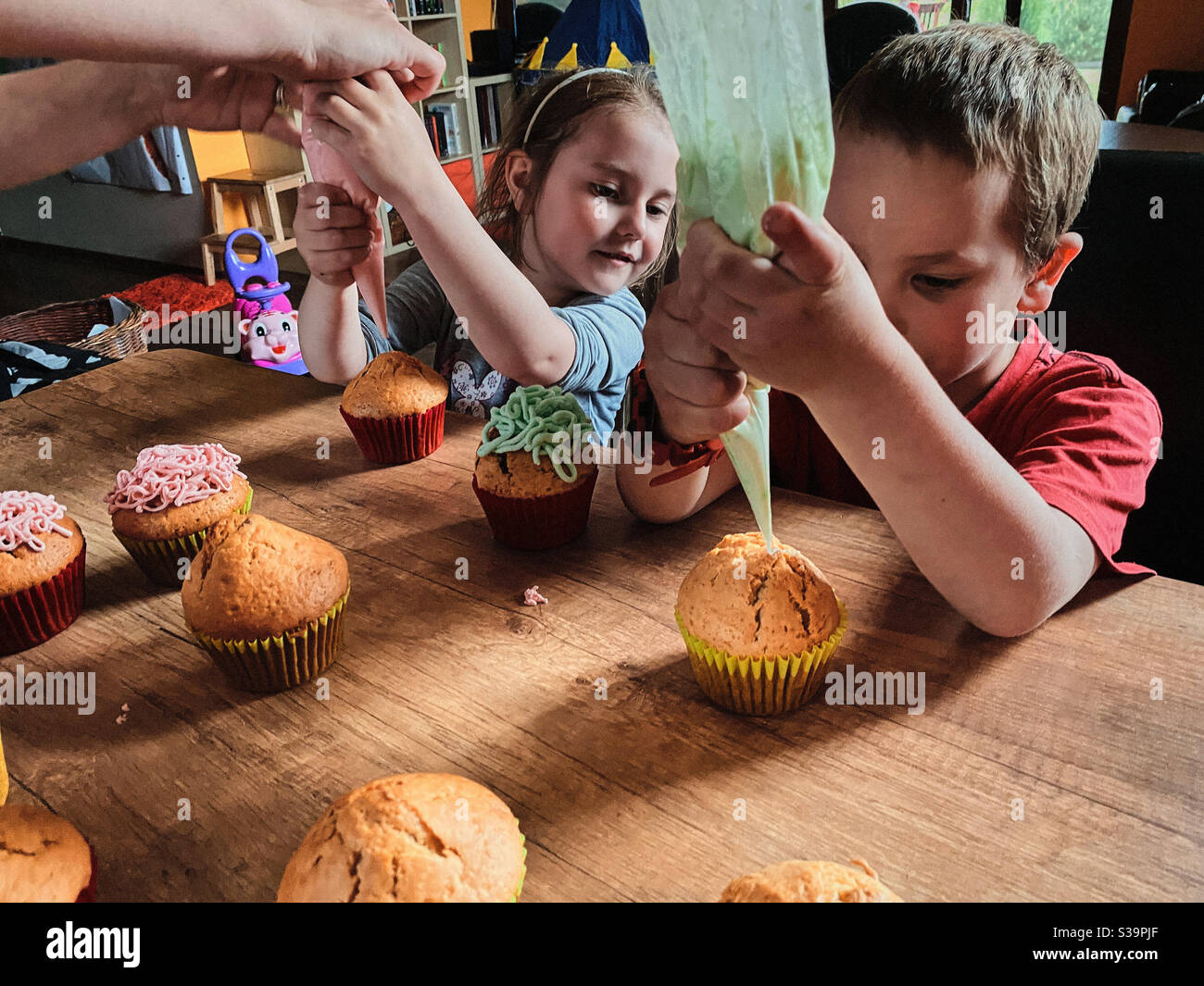 Group of children baking cupcakes, squeezing cream from confectionery