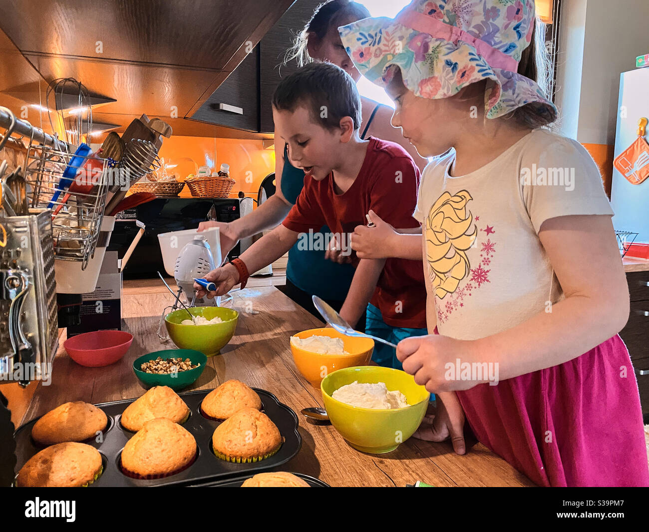 Group of children baking cupcakes, preparing ingredients, toppings, sprinkles for decorating cookies. Kids learning to cook, working together in kitchen at home Stock Photo