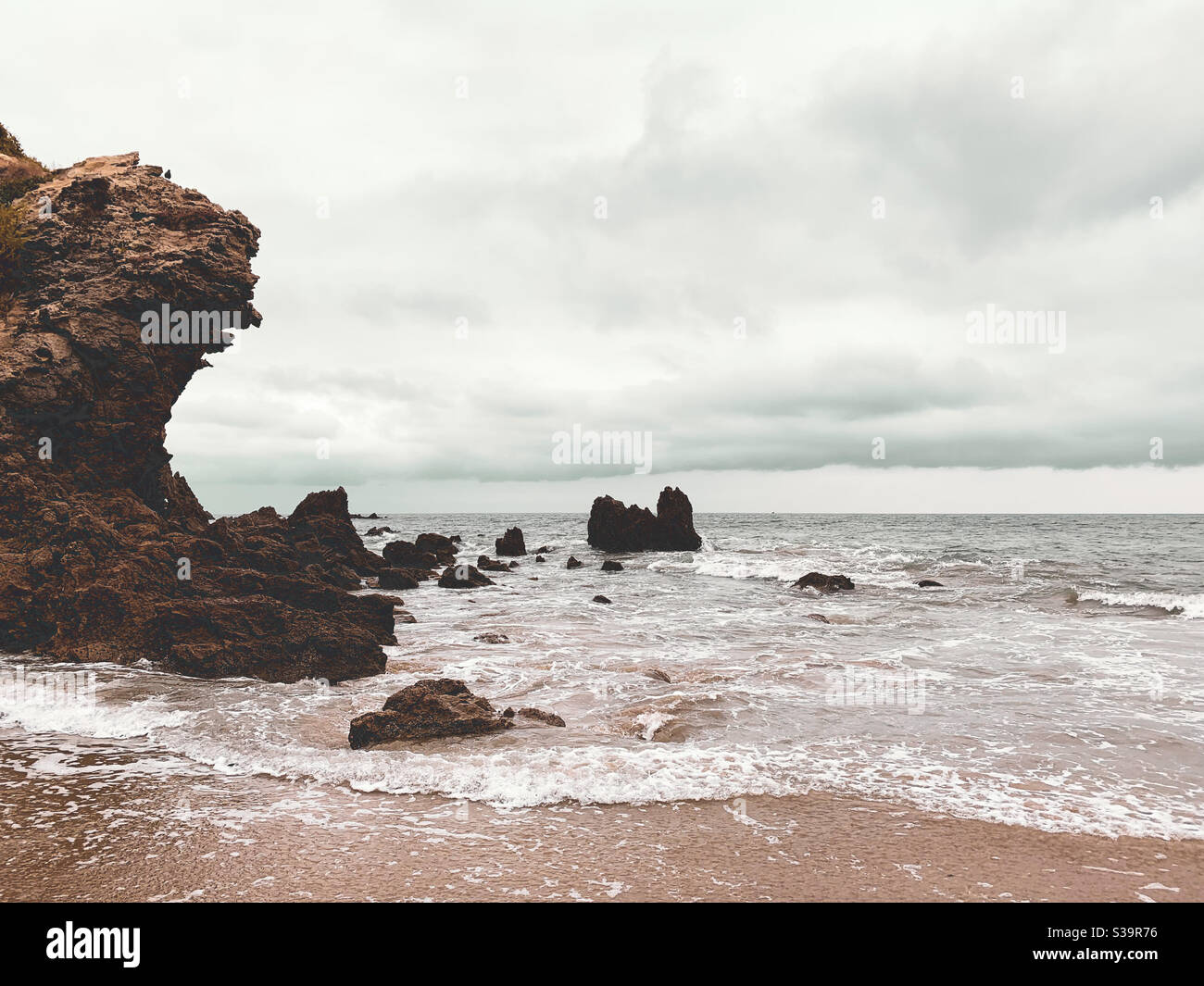 Low angle shot of waves washing up onto beach with dramatic cloud covered sky. - Smartphone Captured Stock Image
