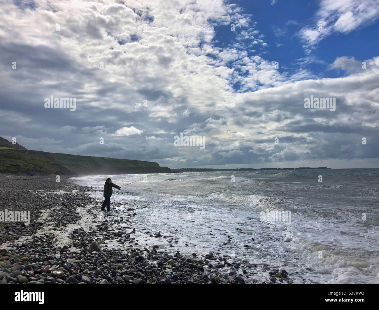Man fishing on Porth Pistyll, North Wales in rough seas, August. - Smartphone Captured Stock Image