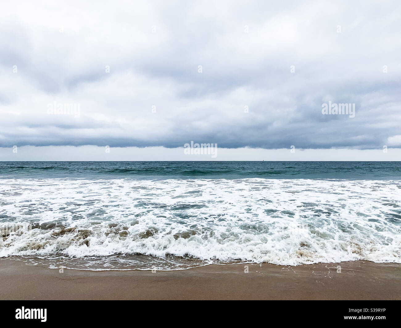Waves washing up onto sandy beach with low clouds above. - Smartphone Captured Stock Image